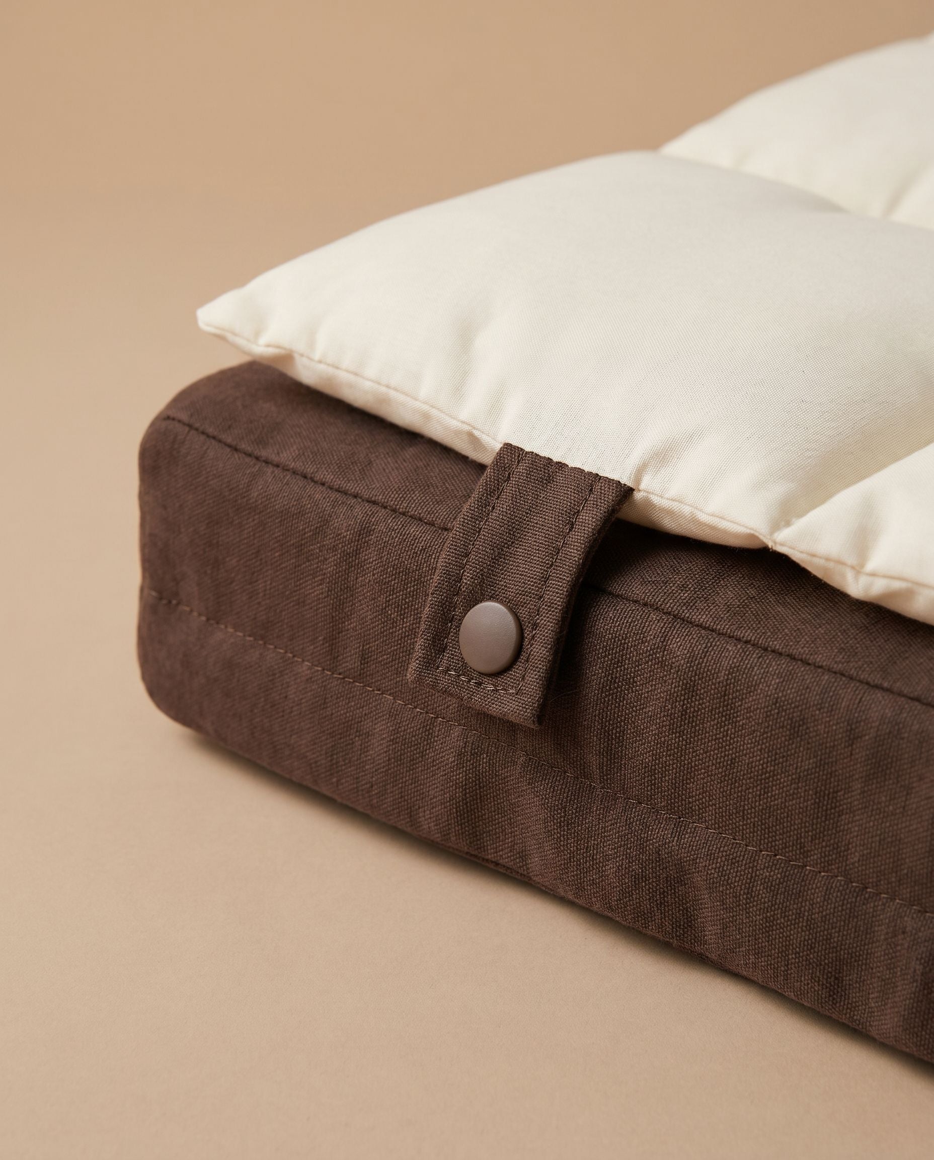 Brown pet bed with a white pillow on a beige background