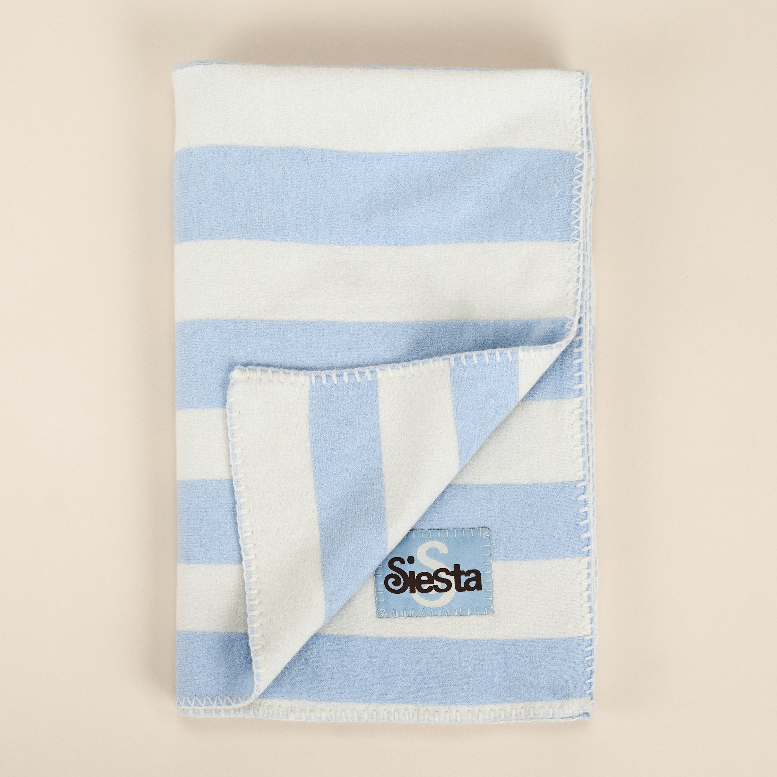 Folded blue and white striped blanket with a logo on a beige background