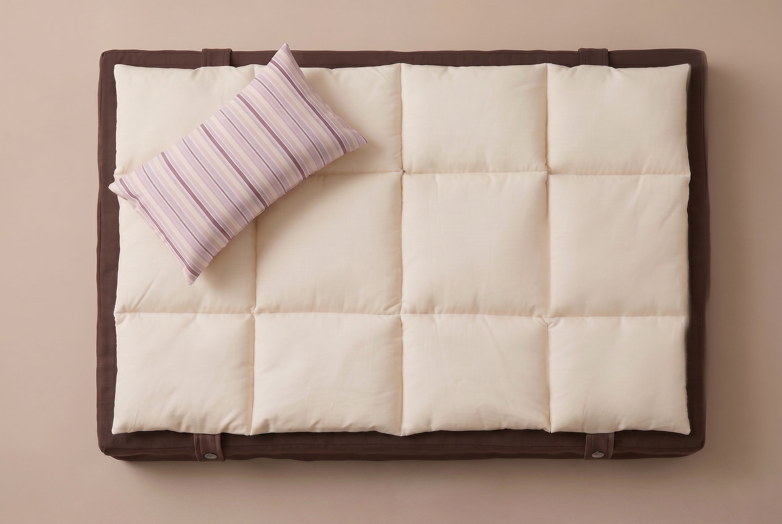 White quilt with brown border and striped pillow on a beige background