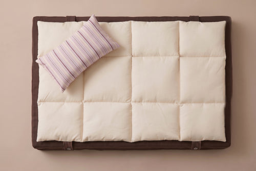 White quilt with brown border and striped pillow on a beige background